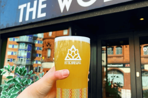hand holding a pint of Attic Brewery beeer in front of the Wolf with sign in the background